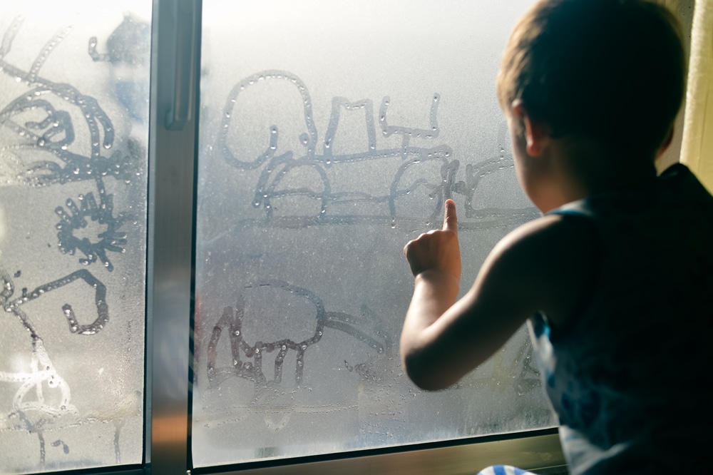 boy drawing on a window with condensation